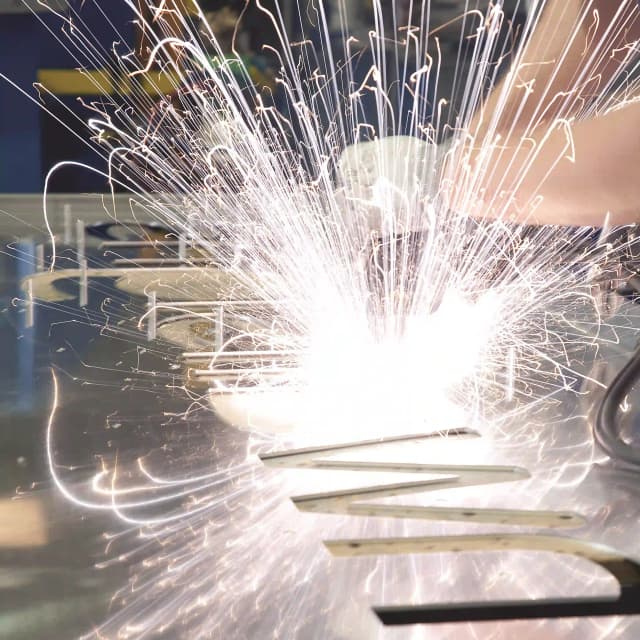 Welding sparks produced from custom sign fabrication. Fixing studs are being spot welded into the rear of a sign tray.